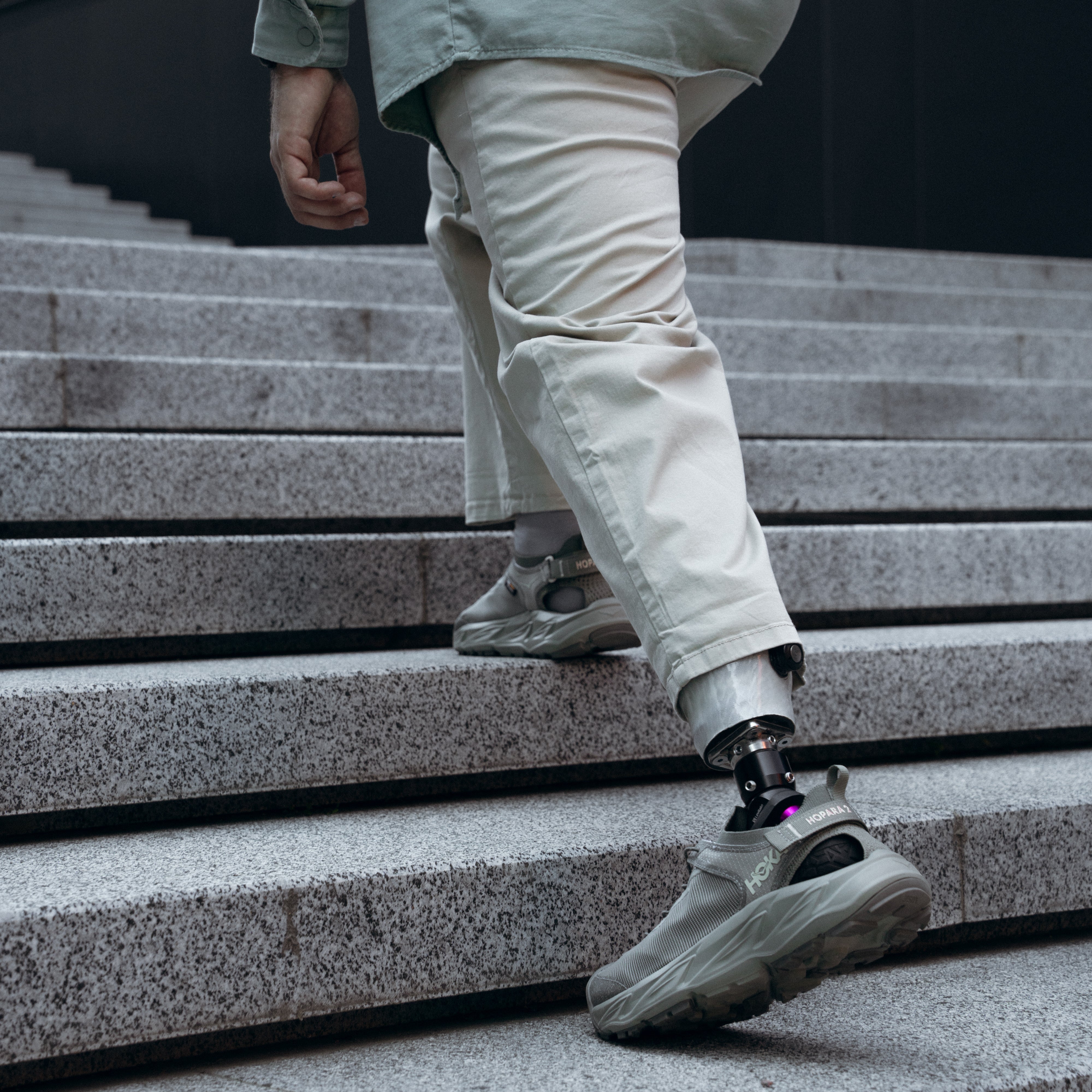Person with a prosthetic leg climbing stairs wearing light-colored pants and shoes.