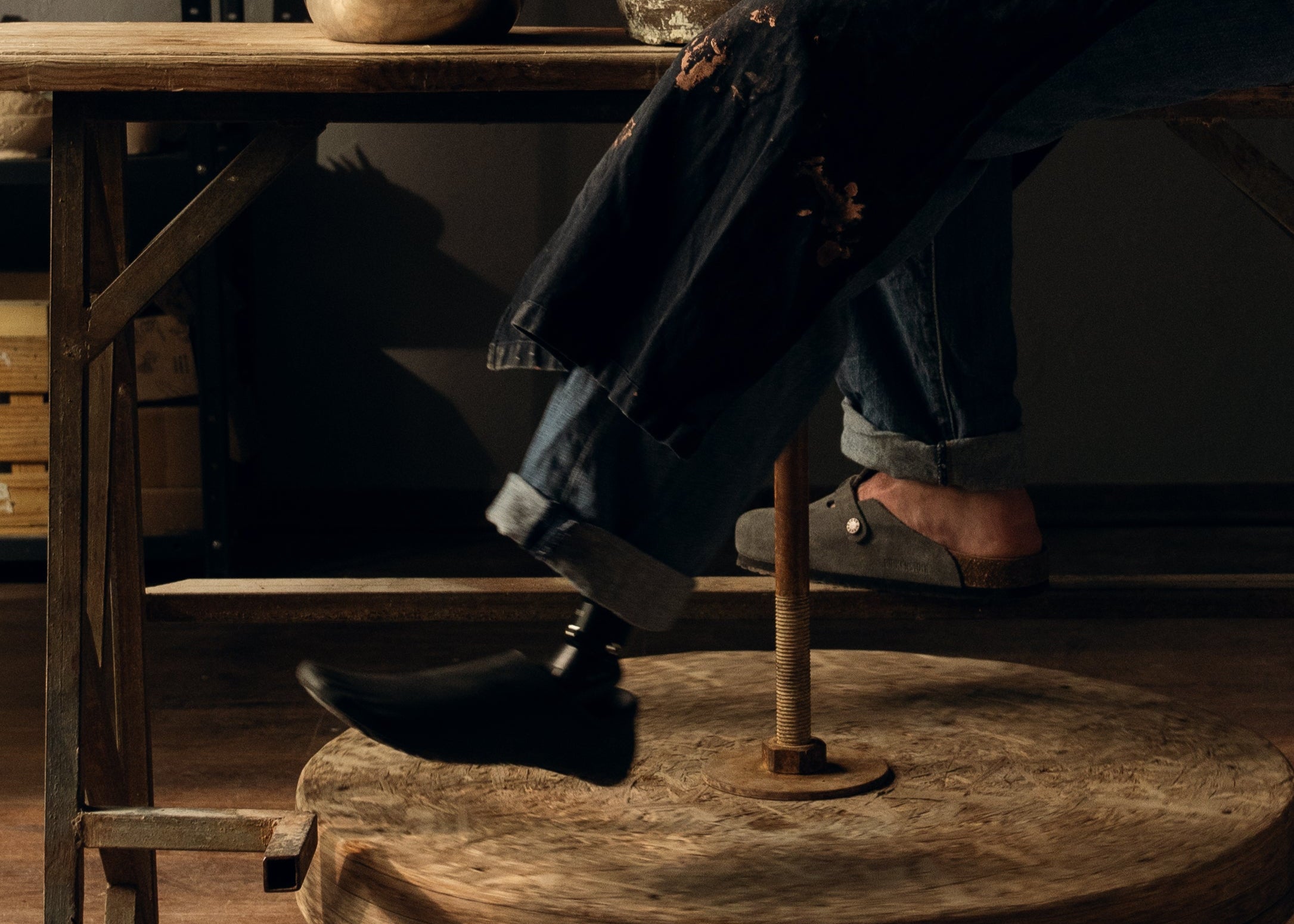 Person with a prosthetic foot sitting at a wooden table with a dark background